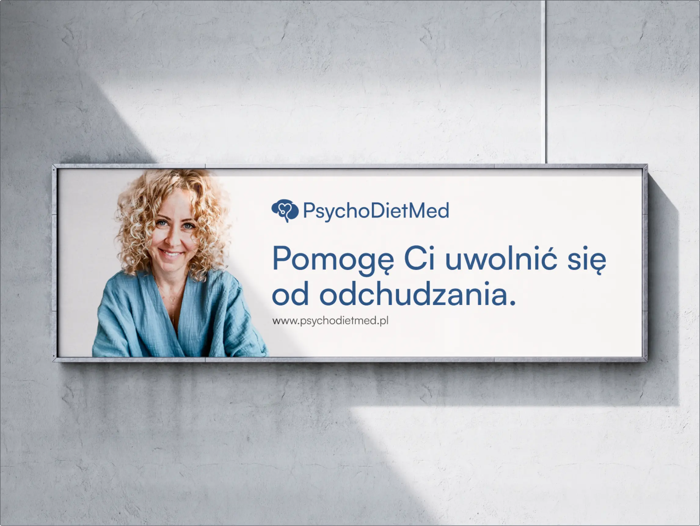 Wizualizacja reklamy kliniki PsychoDietMed na szarej ścianie, na reklamie znajduje się psychodietetyk – blondynka w niebieskiej bluzce