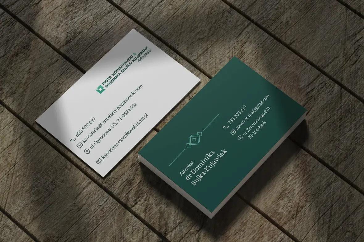 Biało-zielone wizytówki dla kancelarii adwokackiej Nowakowski, które leżą na drewnianym stole